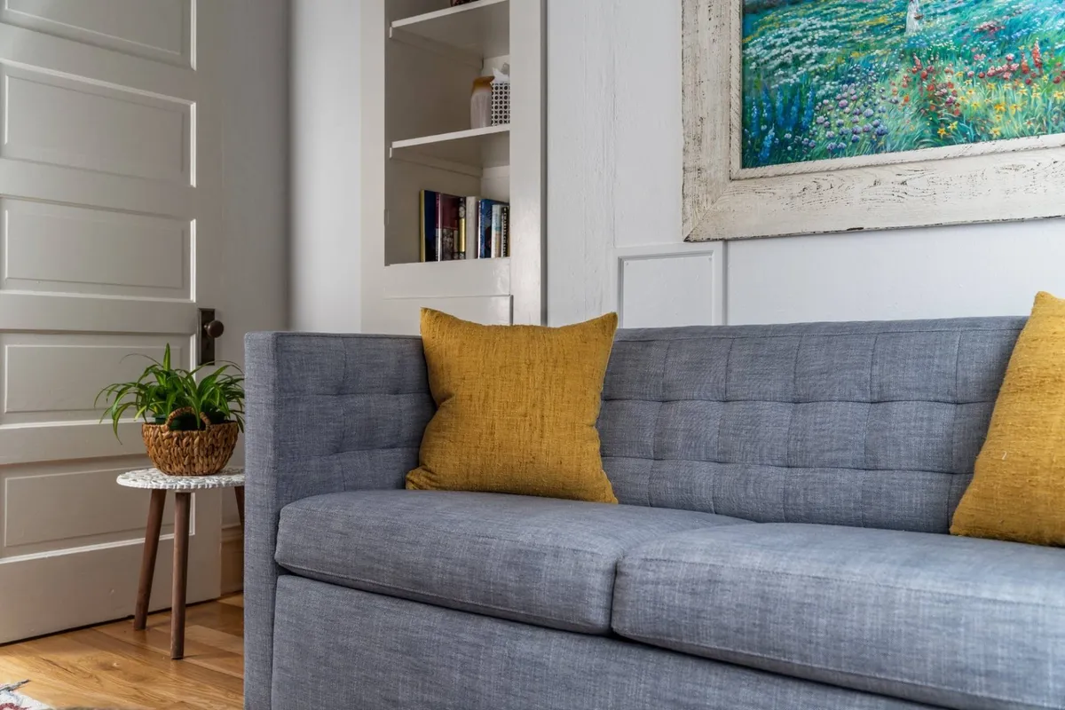A cozy living area with a gray couch adorned with yellow pillows, surrounded by books and framed artwork. The arrangement encourages relaxation, reading, or unwinding after a day spent exploring local attractions.