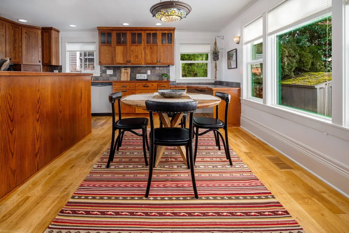 This image features a round dining table set atop a striped area rug, surrounded by warm wooden cabinetry and illuminated by a chandelier. The setting is clearly designed for group meals or casual gatherings, with ample space for families or friends to convene and share time together.