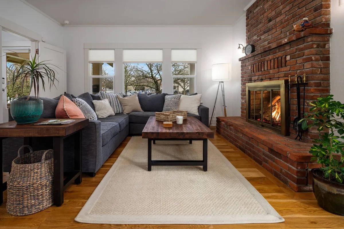 A welcoming living room centered around a cozy fireplace, with a plush sofa, coffee table, and large windows bringing in natural light. The space invites guests to relax, socialize, or enjoy a warm drink—perfect for unwinding after a day out.