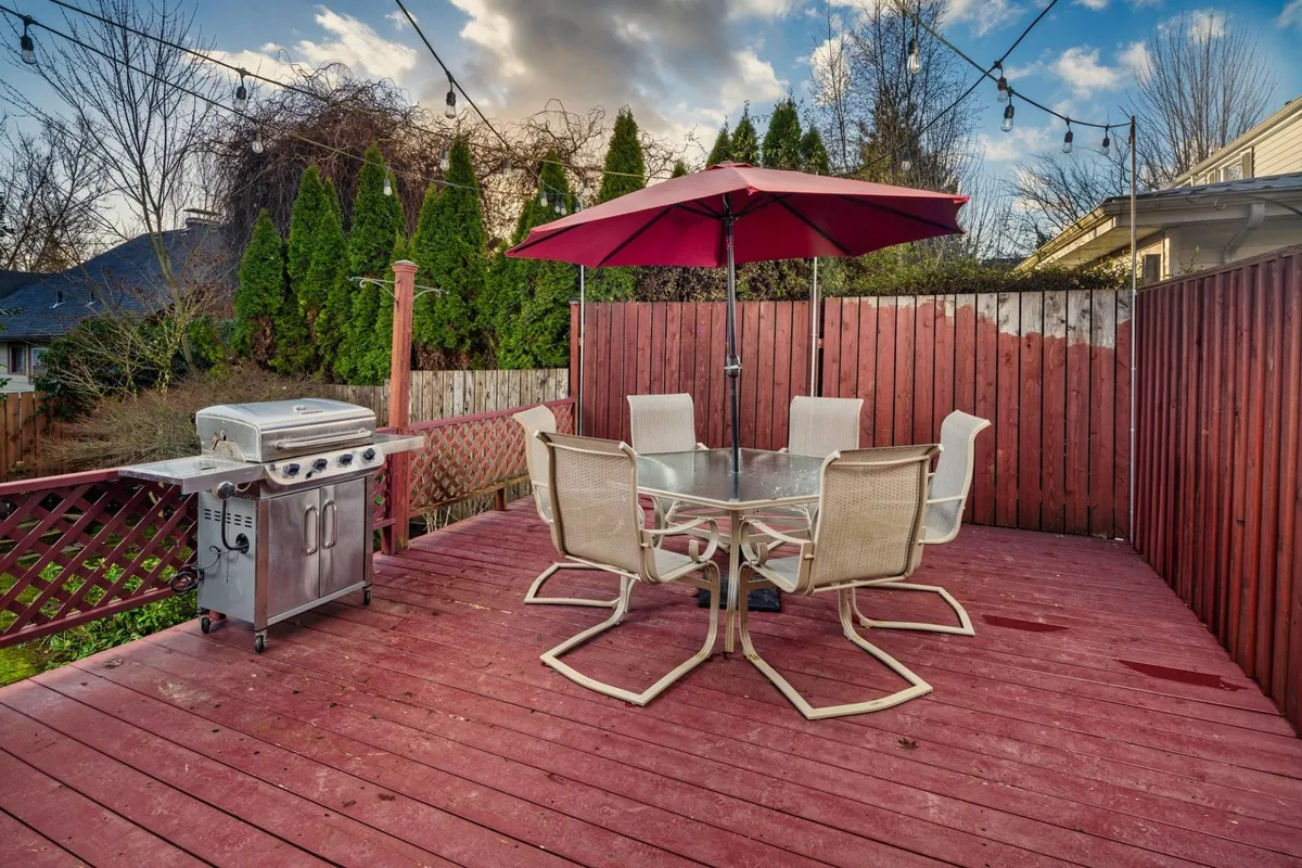 This image features a well-appointed outdoor deck with a dining set, BBQ grill, umbrella, and string (bistro) lights. The scene is framed by a privacy fence, and the space is staged for group gatherings or quiet relaxation. The inviting atmosphere combines elements of open-air dining and casual entertainment.