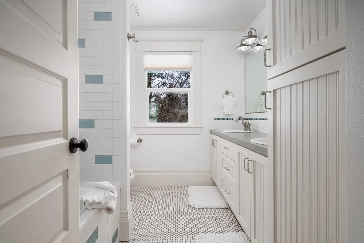 A bright, modern upstairs bathroom featuring a bathtub, sink, and large window that bathes the room in natural light. A large mirror and tranquil decor enhance the sense of space and relaxation.