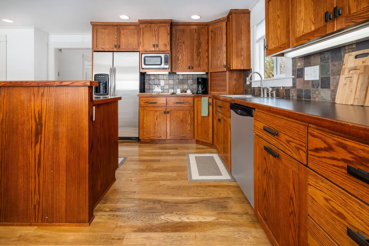 A warm, inviting kitchen scene with wooden cabinetry, stainless steel appliances, and a generous countertop, ideal for meal prepping or serving. The ambiance encourages both cooking and conversations, supporting culinary and social activities.